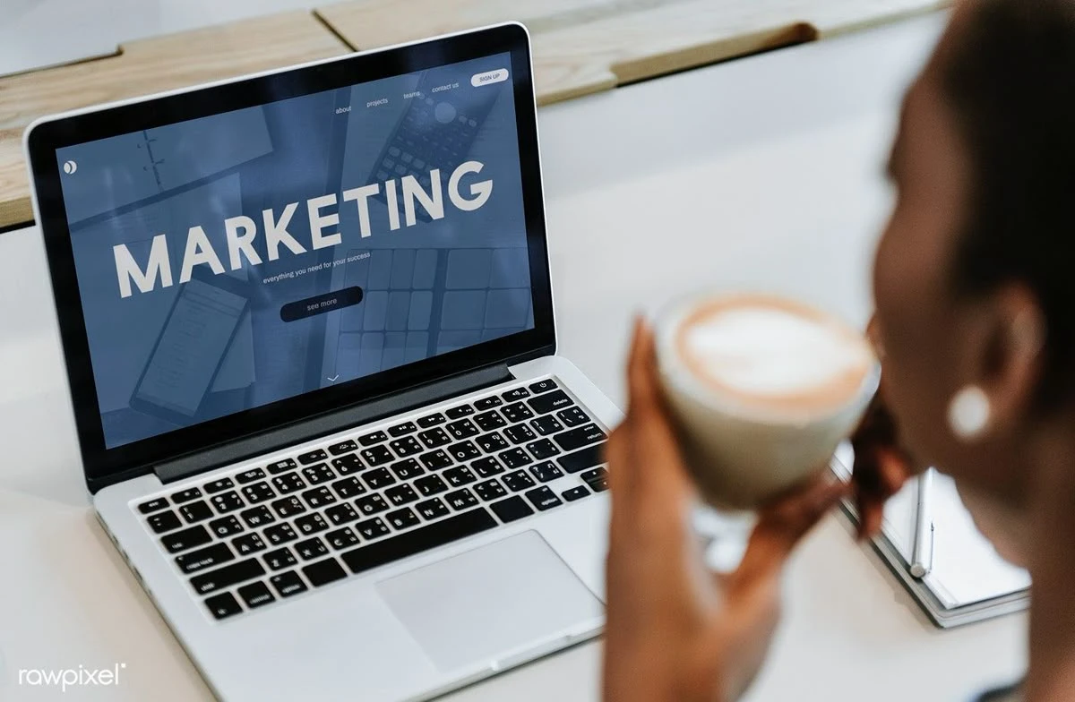 Digital marketing strategist in Malappuram working on a laptop with a visible ‘Marketing’ screen, holding a coffee cup at a modern workspace