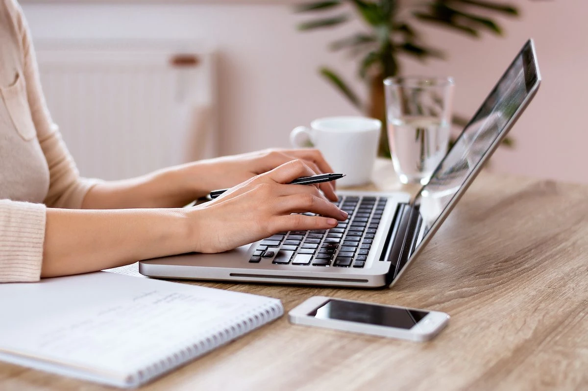 Freelance digital marketing analyst in Malappuram working at a wooden desk with a laptop, notebook, pen, and smartphone, accompanied by a glass of water and coffee cup—depicting a productive workspace.